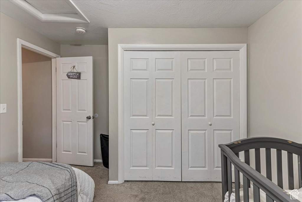 Bedroom with a closet, light colored carpet, and a crib