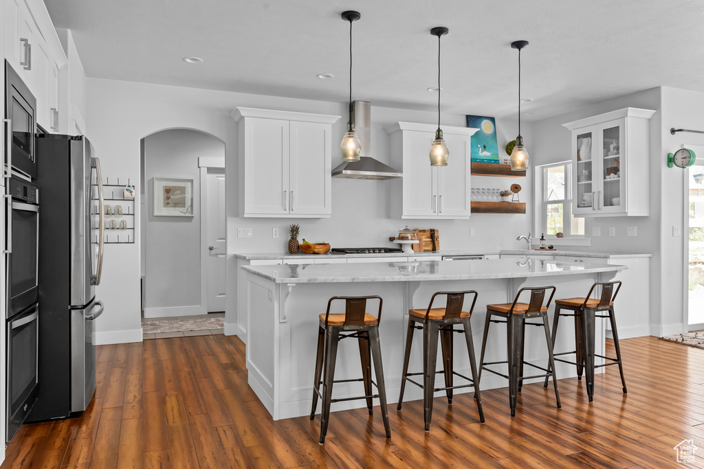 Kitchen featuring a center island, a breakfast bar area, wall chimney exhaust hood, white cabinets, and dark hardwood / wood-style flooring