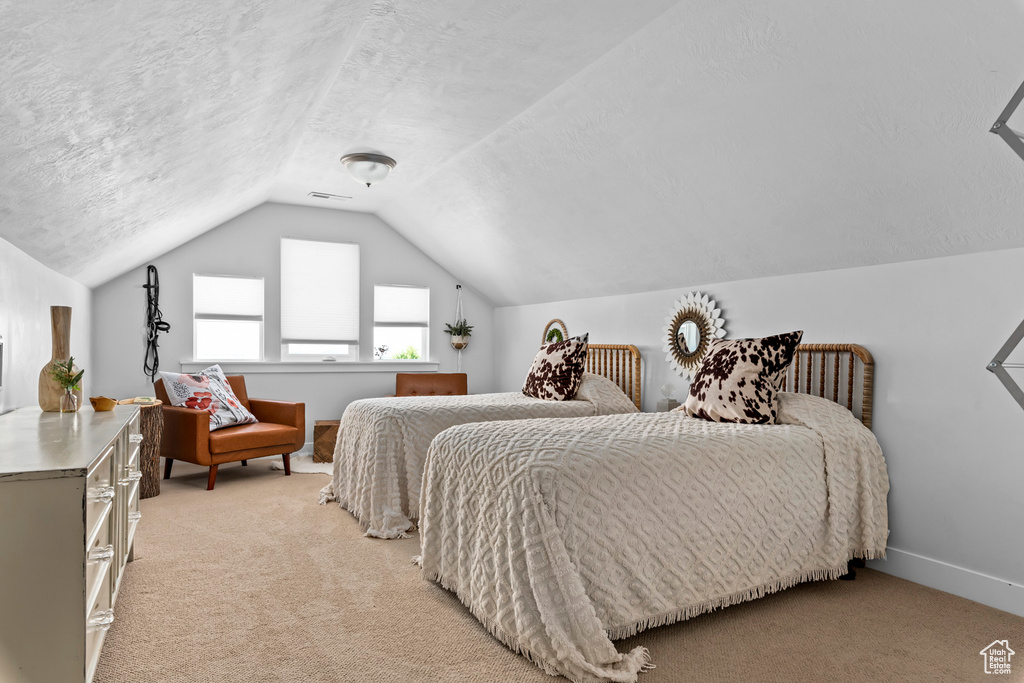 Bedroom featuring a textured ceiling, vaulted ceiling, and light colored carpet