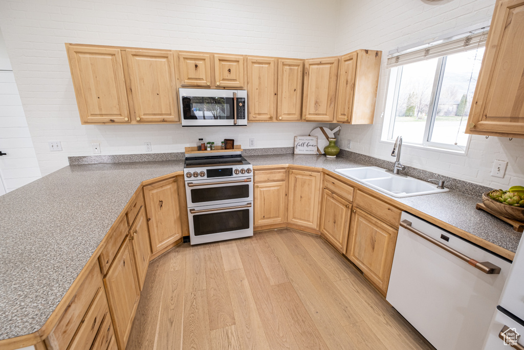 Kitchen with light brown cabinets, light hardwood / wood-style floors, sink, dishwasher, and range with two ovens
