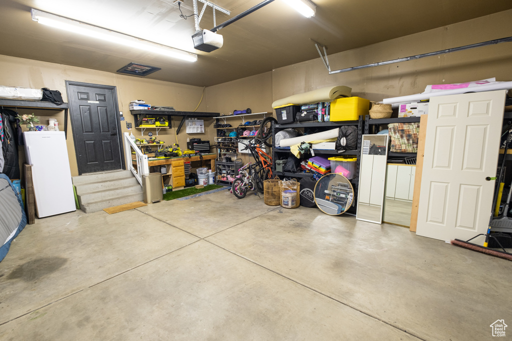 Garage with a garage door opener, white fridge, and a workshop area