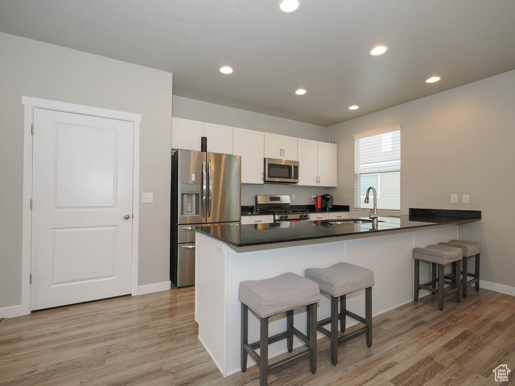 Kitchen featuring white cabinetry, a breakfast bar, light hardwood / wood-style floors, sink, and stainless steel appliances