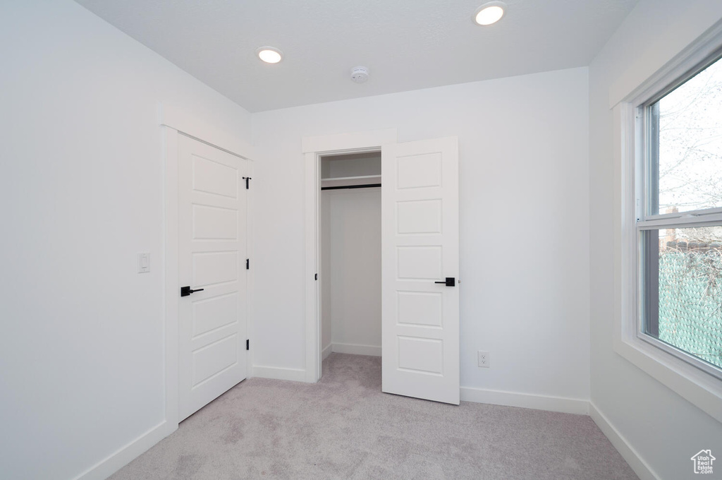 Unfurnished bedroom featuring a closet, light carpet, and multiple windows