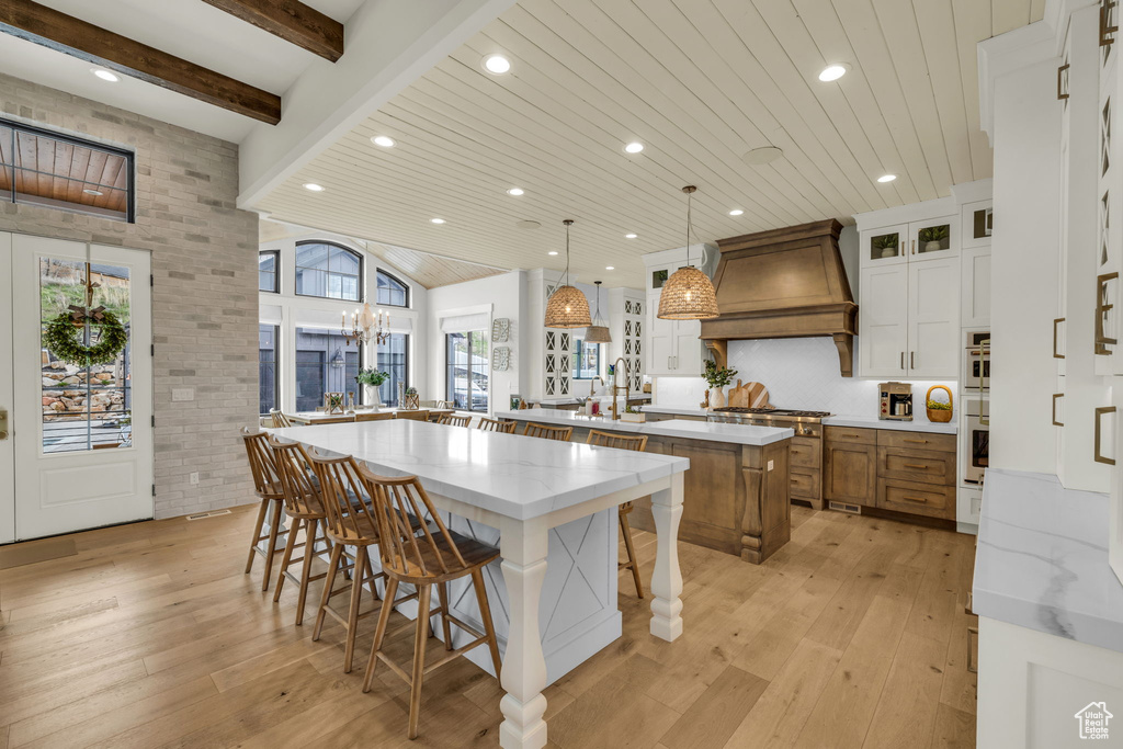 Kitchen featuring a center island with sink, light wood-type flooring, a wealth of natural light, and premium range hood