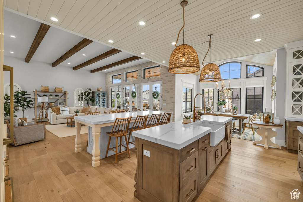 Kitchen with decorative light fixtures, light stone countertops, a center island with sink, light wood-type flooring, and sink