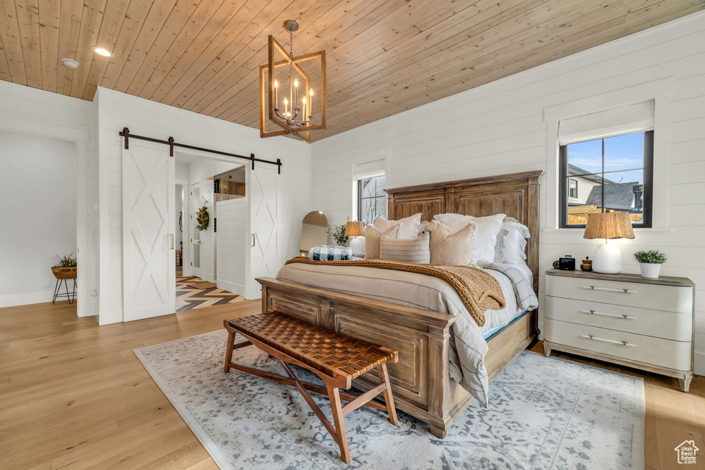 Bedroom with a barn door, wood ceiling, an inviting chandelier, and light wood-type flooring