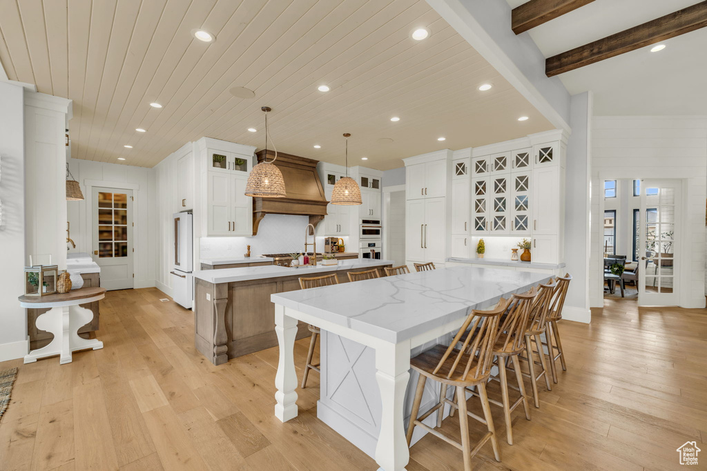 Kitchen featuring a large island, light stone countertops, custom exhaust hood, white cabinetry, and light wood-type flooring