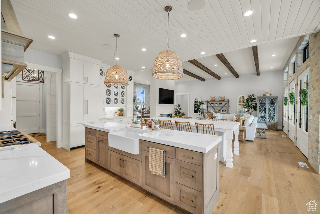 Kitchen with white cabinetry, hanging light fixtures, beamed ceiling, light hardwood / wood-style flooring, and an island with sink