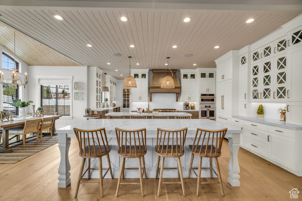Kitchen with a kitchen bar, a spacious island, custom exhaust hood, and white cabinetry