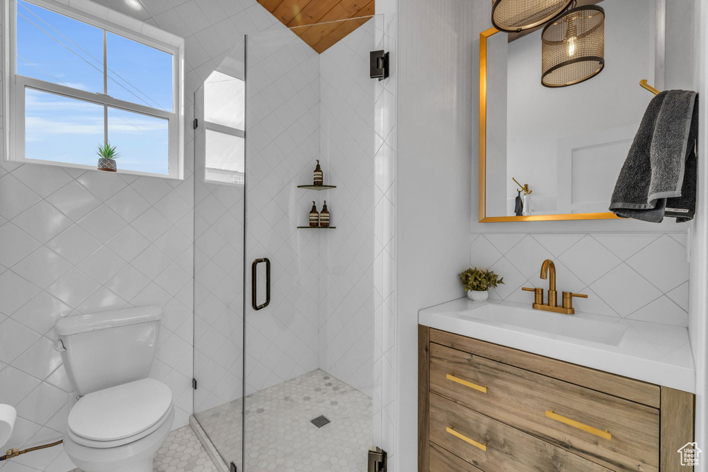 Bathroom featuring an enclosed shower, vanity, tile walls, tile flooring, and toilet