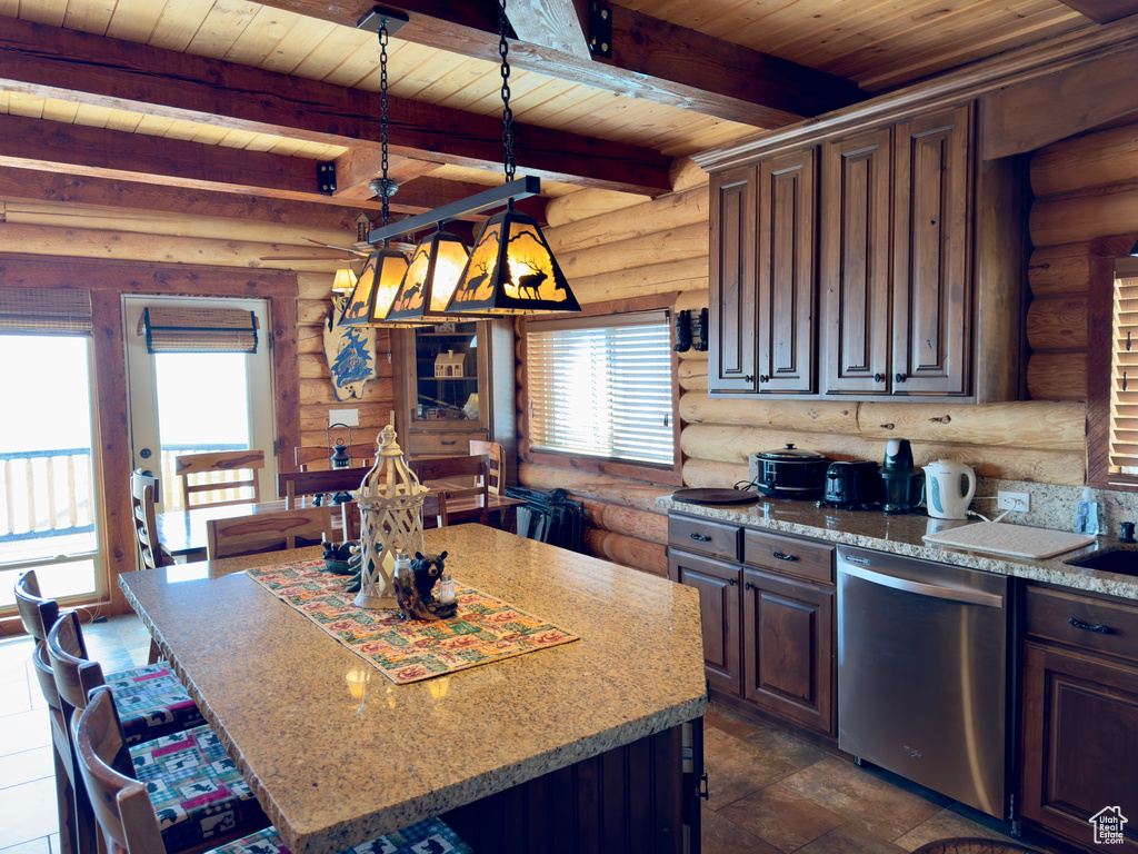 Kitchen featuring decorative light fixtures, a kitchen island, stainless steel dishwasher, log walls, and beam ceiling