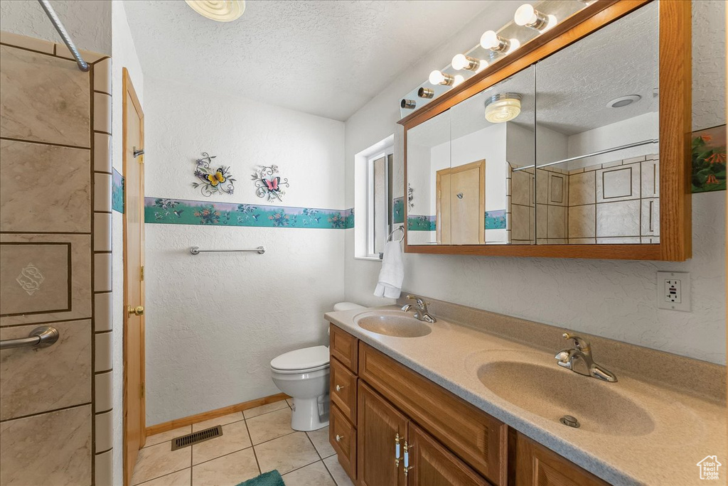 Bathroom with tile floors, toilet, dual vanity, and a textured ceiling