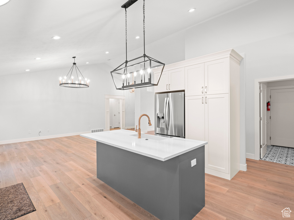 Kitchen with an island with sink, pendant lighting, stainless steel fridge with ice dispenser, light hardwood / wood-style flooring, and white cabinetry