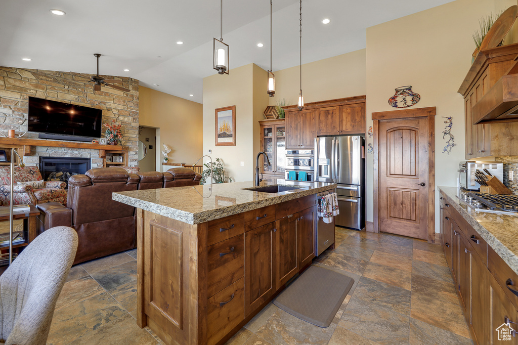 Kitchen featuring ceiling fan, an island with sink, hanging light fixtures, sink, and a stone fireplace