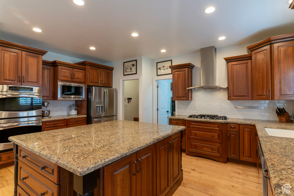 Kitchen featuring light hardwood / wood-style flooring, stainless steel appliances, tasteful backsplash, a kitchen island, and wall chimney exhaust hood