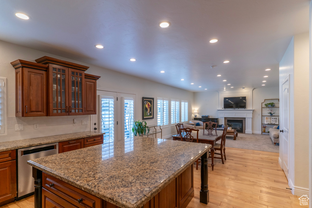 Kitchen with light stone countertops, light wood-type flooring, dishwasher, a kitchen island, and tasteful backsplash