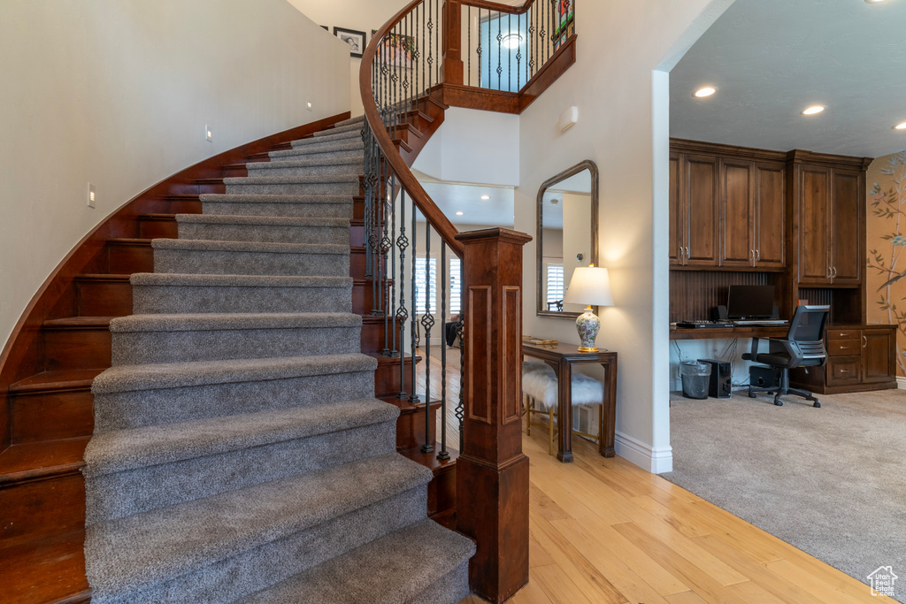 Stairs featuring built in desk, a high ceiling, and light hardwood / wood-style flooring