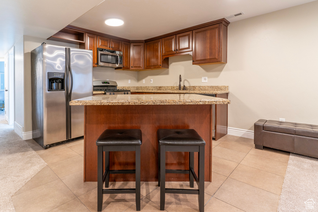 Kitchen with light tile floors, light stone countertops, a breakfast bar area, and stainless steel appliances