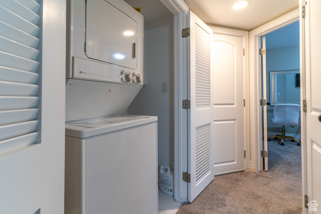 Laundry area featuring stacked washer and clothes dryer and light colored carpet