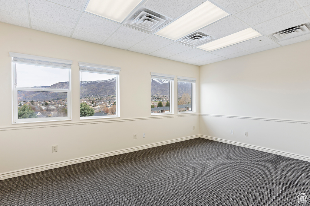 Unfurnished room featuring plenty of natural light, dark carpet, a mountain view, and a drop ceiling