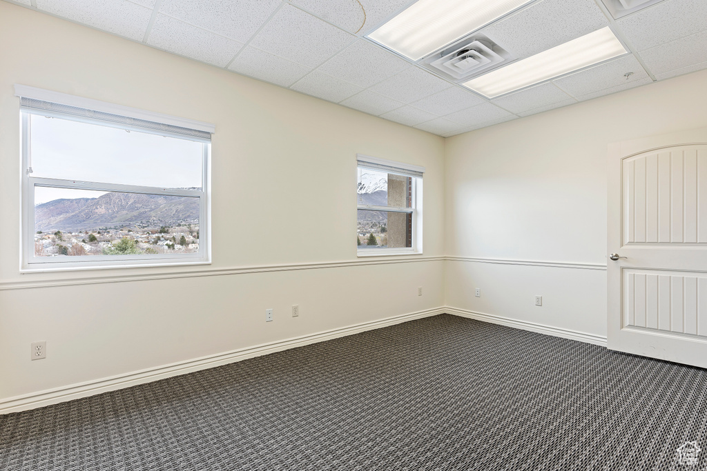 Unfurnished room with a drop ceiling, a mountain view, and dark colored carpet