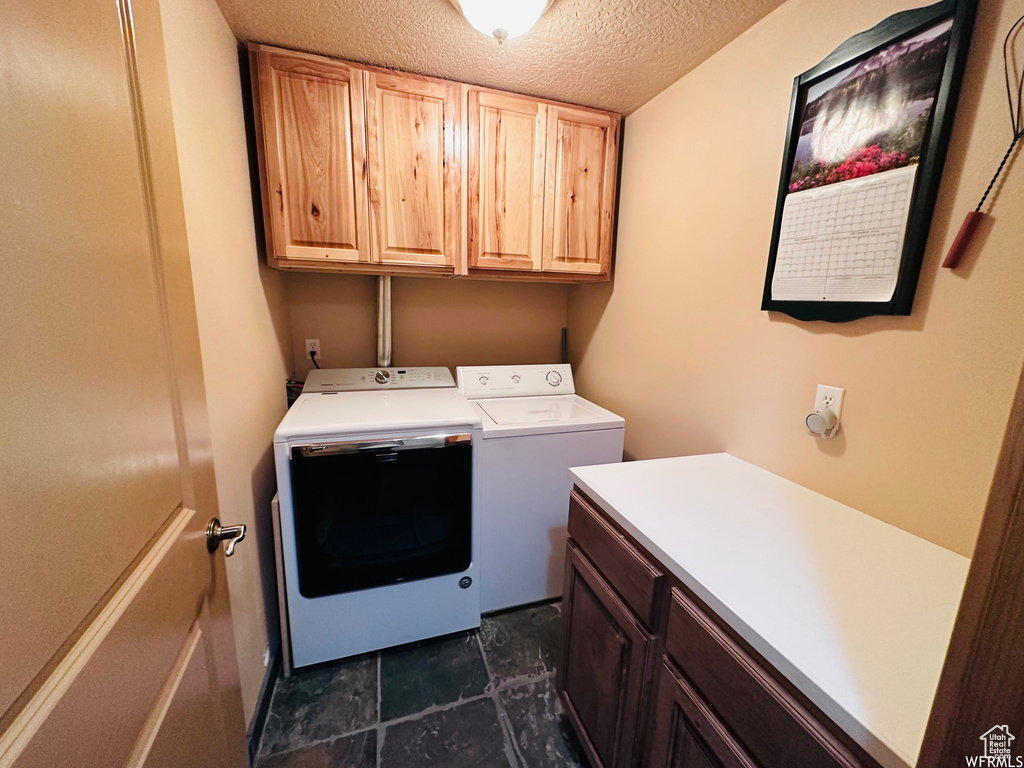 Laundry area with cabinets, dark tile floors, a textured ceiling, and washing machine and clothes dryer