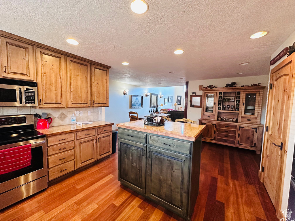 Kitchen featuring hardwood / wood-style floors, appliances with stainless steel finishes, tasteful backsplash, a textured ceiling, and a center island
