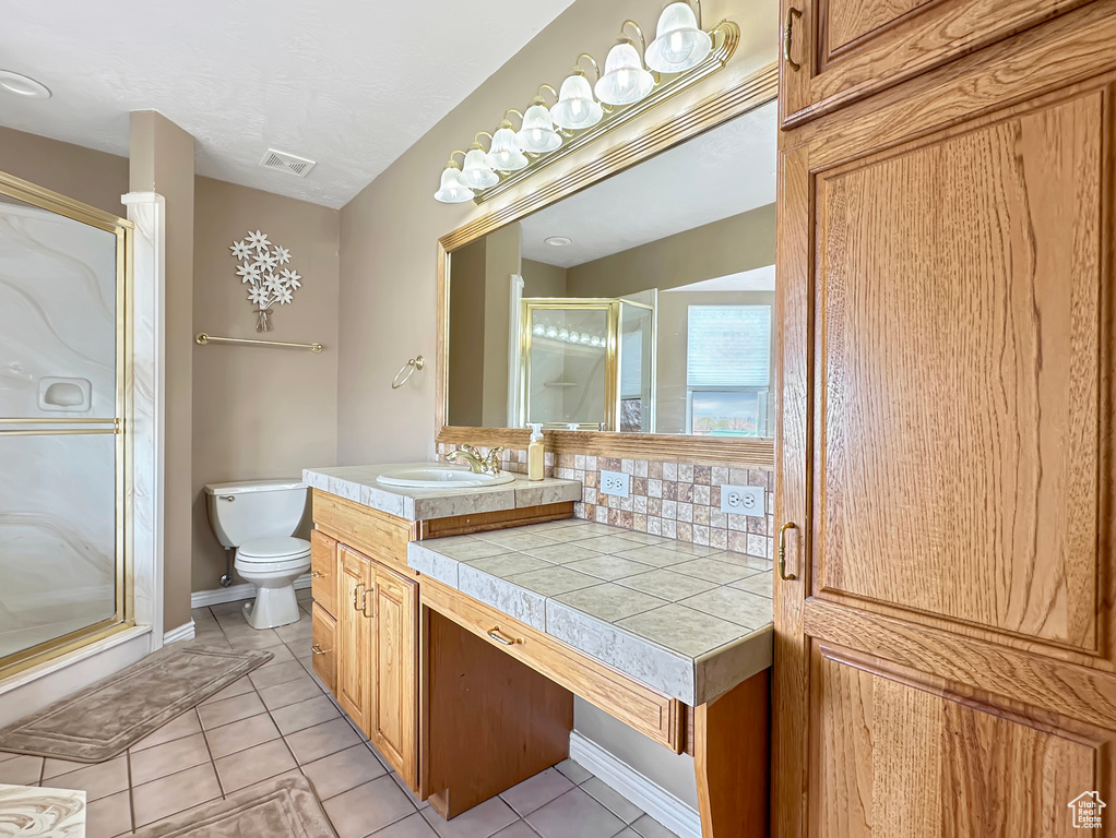 Bathroom featuring toilet, large vanity, tile floors, and a shower with shower door