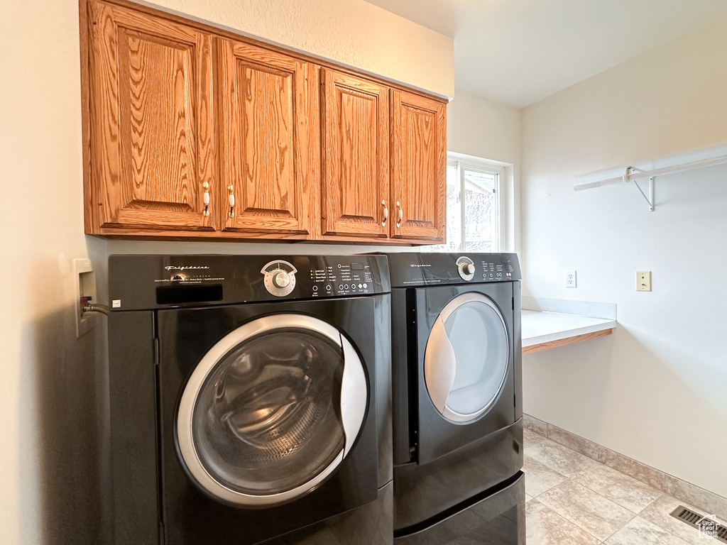 Clothes washing area featuring washer and clothes dryer, light tile flooring, and cabinets