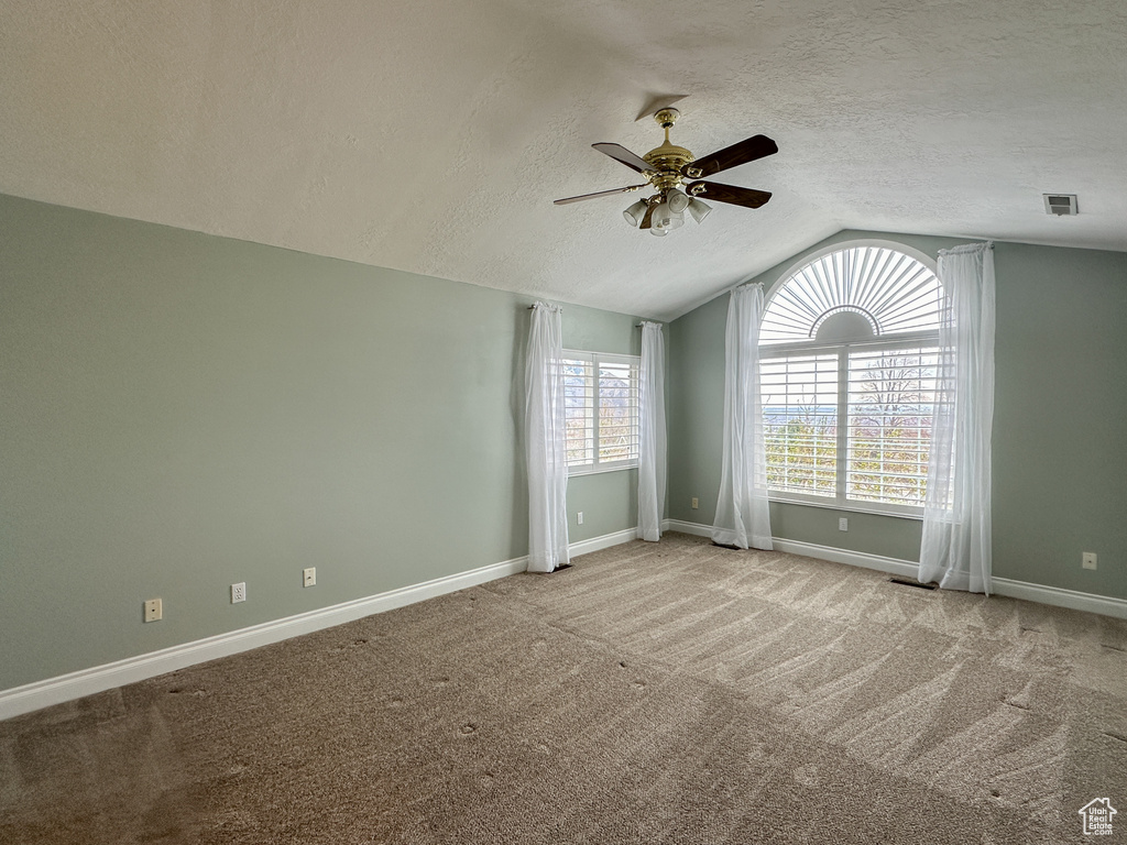 Empty room featuring light carpet, a textured ceiling, ceiling fan, and vaulted ceiling