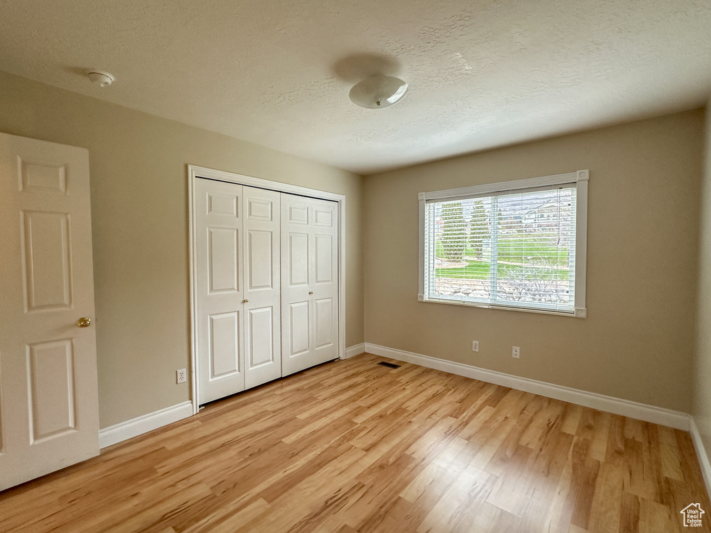 Unfurnished bedroom featuring light hardwood / wood-style floors, a closet, and a textured ceiling