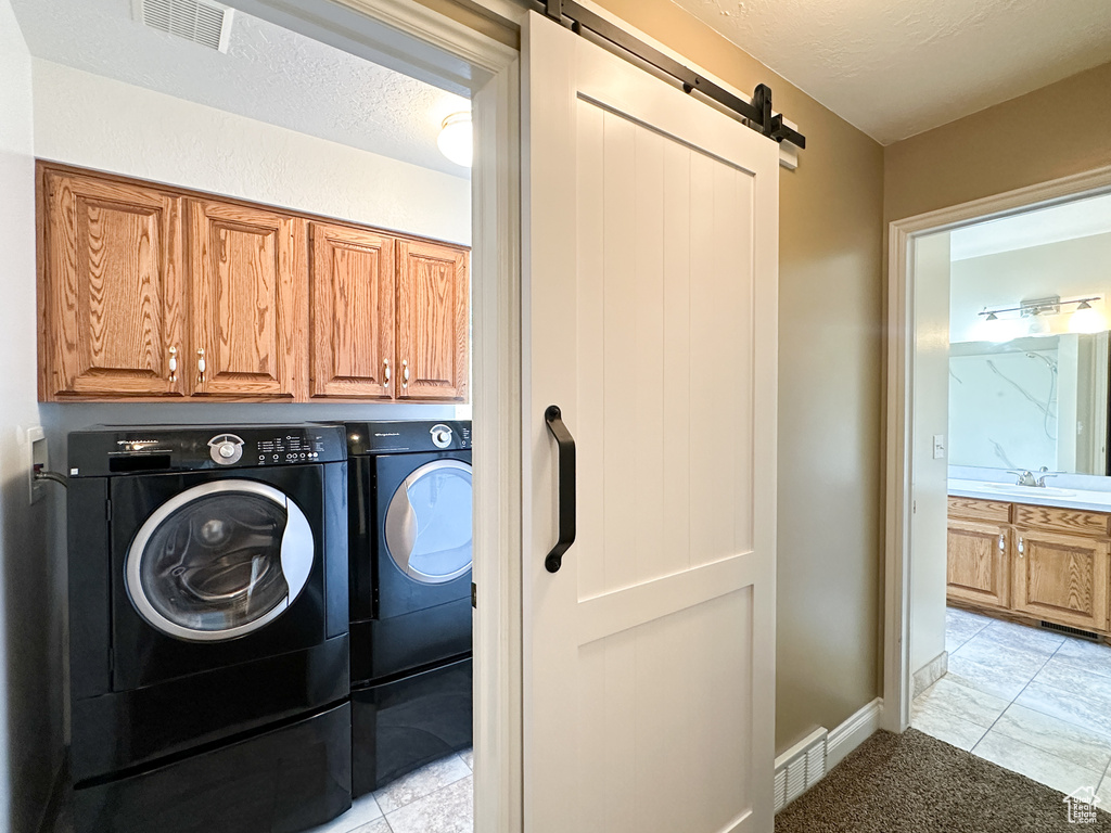 Laundry room featuring a barn door, independent washer and dryer, light tile floors, and cabinets