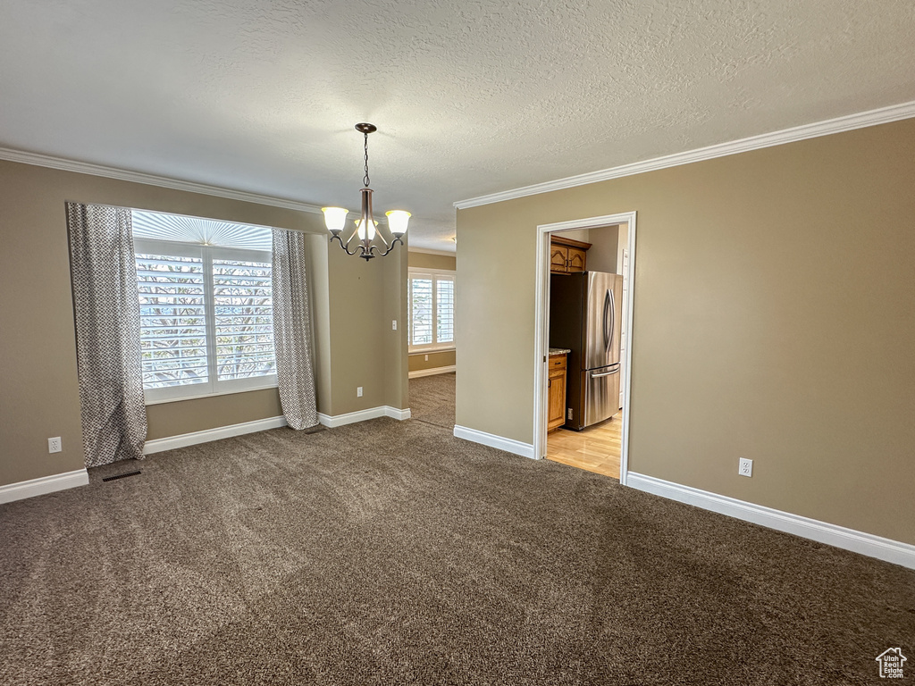 Empty room with a chandelier, crown molding, and light colored carpet