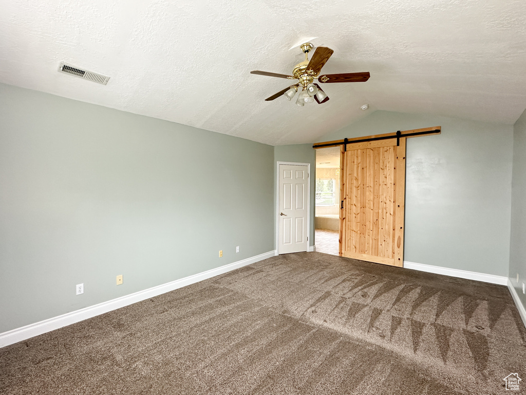 Unfurnished bedroom featuring ceiling fan, carpet, vaulted ceiling, a barn door, and a textured ceiling