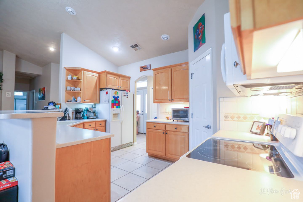 Kitchen with light tile floors, backsplash, range, vaulted ceiling, and white fridge with ice dispenser