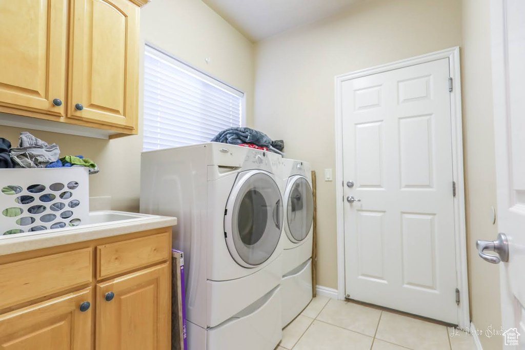 Clothes washing area with separate washer and dryer, cabinets, and light tile flooring