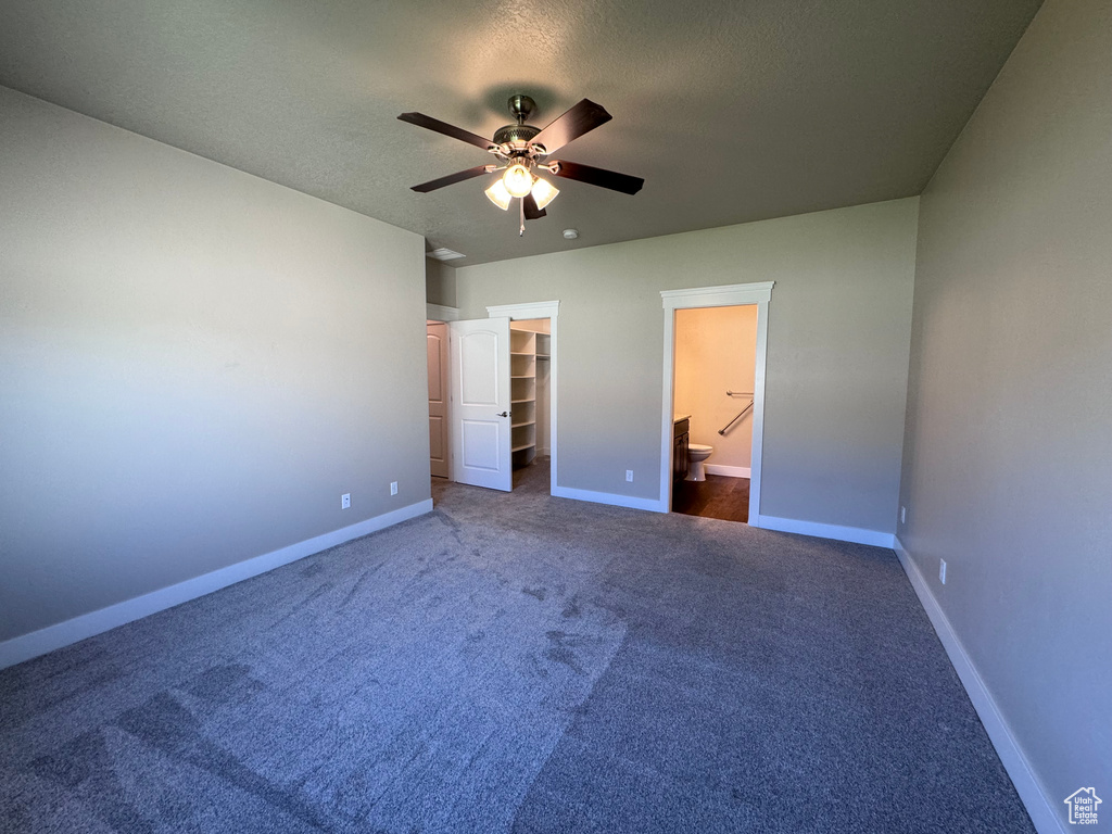 Unfurnished bedroom with ceiling fan, a closet, dark carpet, a walk in closet, and connected bathroom