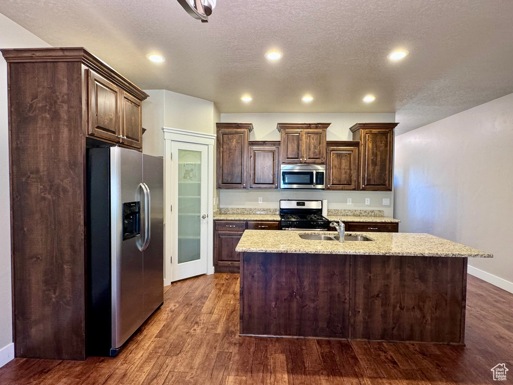Kitchen featuring sink, appliances with stainless steel finishes, an island with sink, and dark wood-type flooring