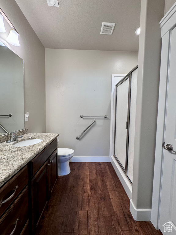 Bathroom with a textured ceiling, toilet, wood-type flooring, vanity, and a shower with door