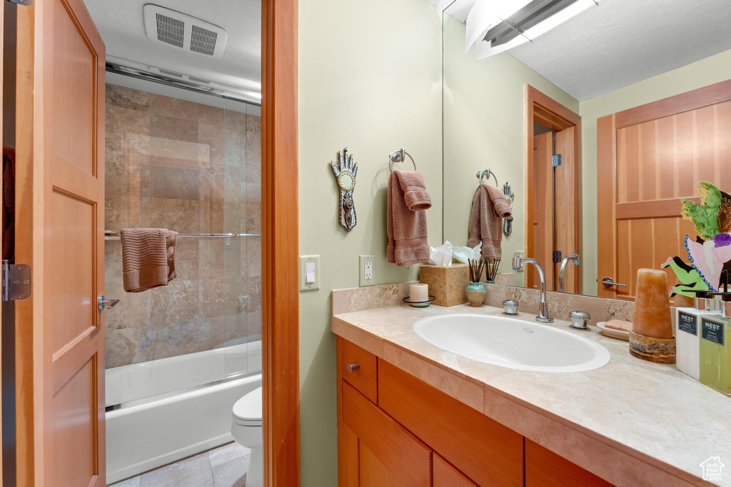 Full bathroom featuring tile flooring, bath / shower combo with glass door, vanity with extensive cabinet space, and toilet