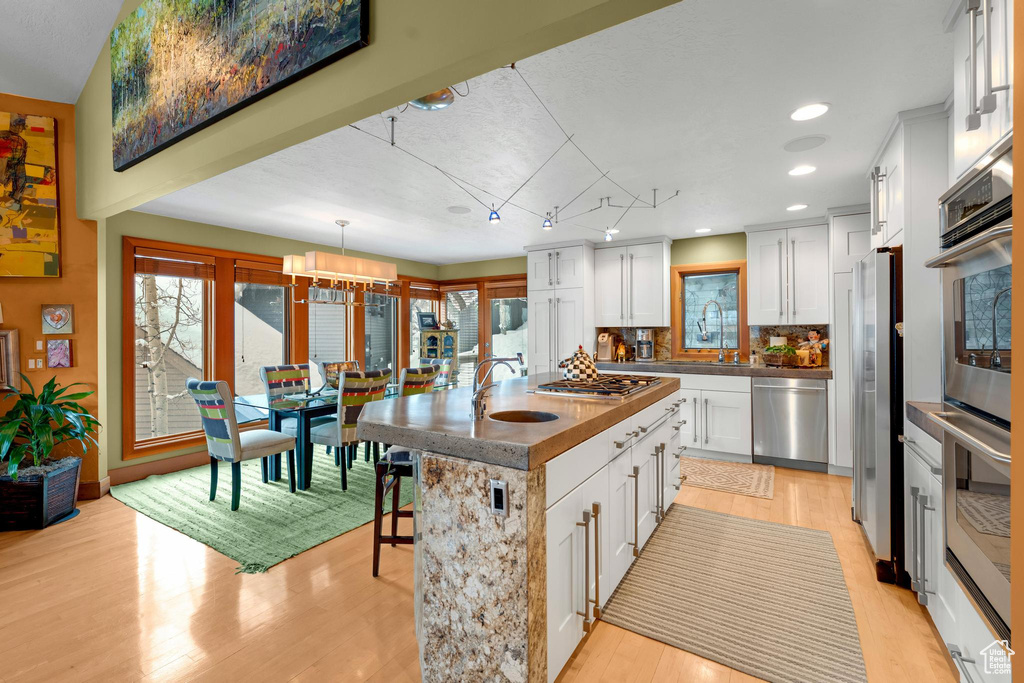 Kitchen featuring white cabinets, an island with sink, plenty of natural light, and stainless steel appliances