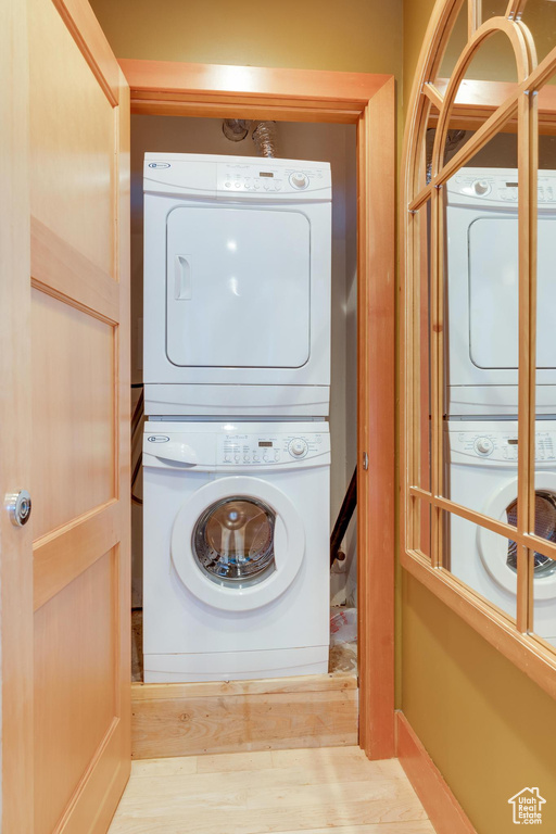 Clothes washing area with stacked washer and clothes dryer and light hardwood / wood-style floors