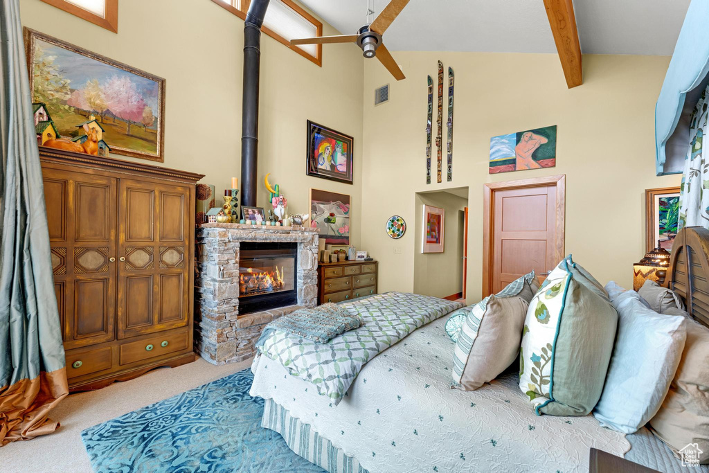 Bedroom with ceiling fan, beamed ceiling, high vaulted ceiling, a stone fireplace, and light colored carpet
