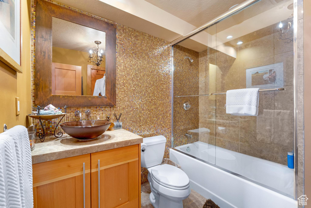 Full bathroom featuring a chandelier, toilet, vanity, tasteful backsplash, and combined bath / shower with glass door