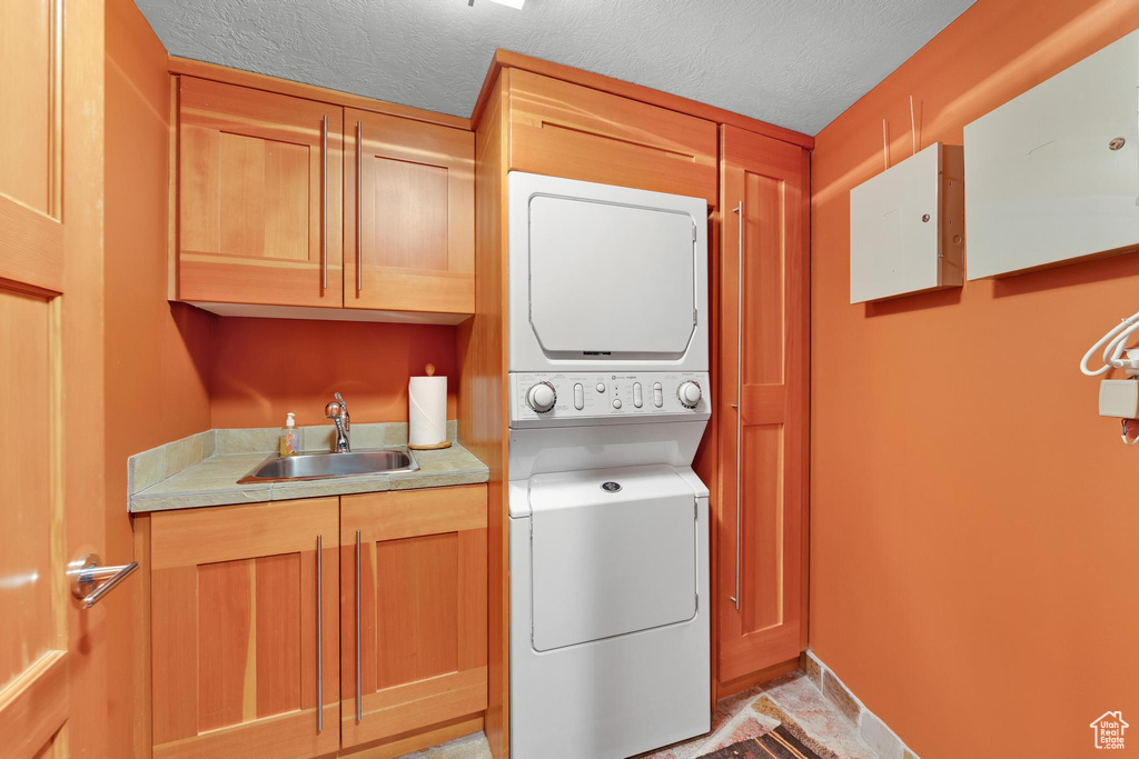 Clothes washing area with stacked washer / dryer, cabinets, sink, light tile floors, and a textured ceiling