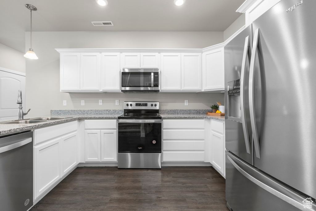Kitchen featuring white cabinets, light stone countertops, stainless steel appliances, and dark wood-type flooring