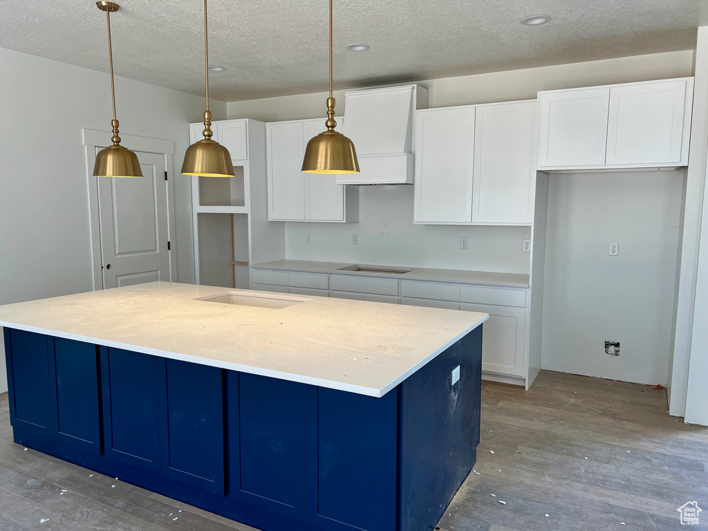 Kitchen featuring a kitchen island, pendant lighting, hardwood / wood-style flooring, and white cabinetry