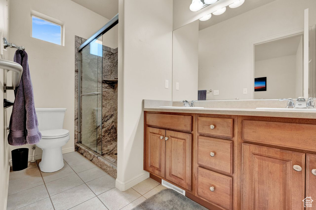 Bathroom featuring toilet, double vanity, tile flooring, and a shower with door