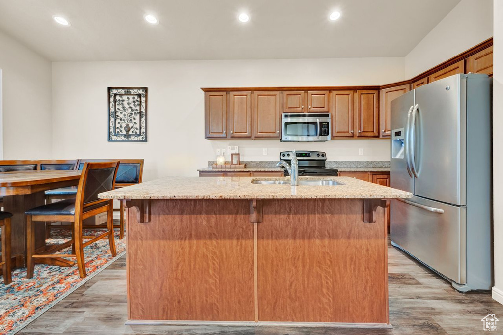 Kitchen featuring a center island with sink, appliances with stainless steel finishes, light stone counters, and light hardwood / wood-style flooring