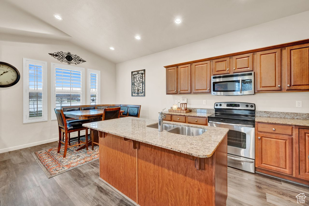 Kitchen featuring light stone countertops, appliances with stainless steel finishes, sink, light hardwood / wood-style flooring, and a center island with sink